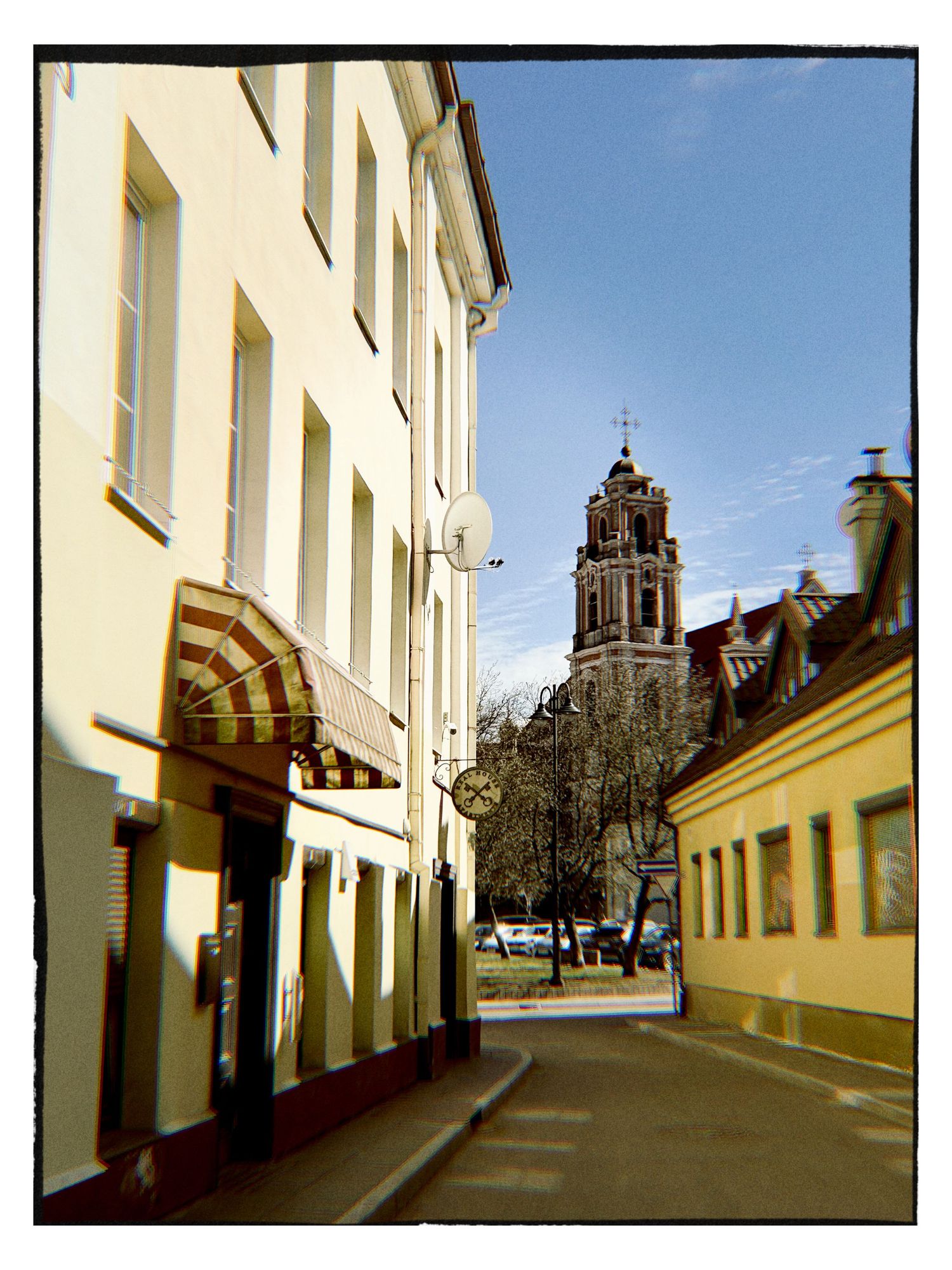 Narrow European street with yellow buildings and a historic church bell tower under a clear blue sky.