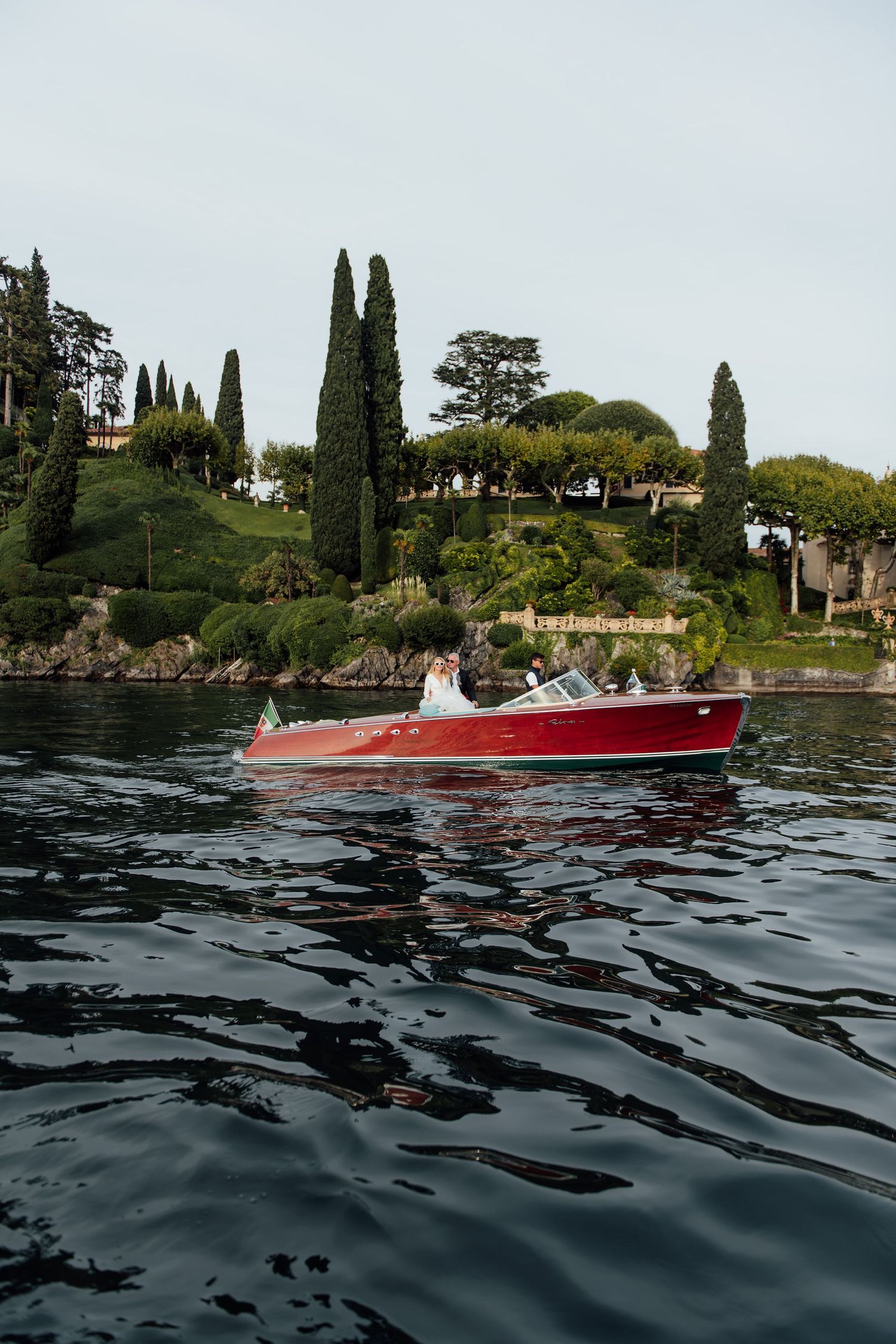 A series of photos showing a red speedboat cruising along the dark waters near a Mediterranean coastline with cypress trees.