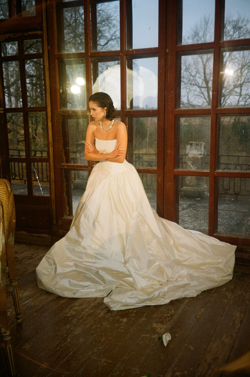 Bride in strapless white ball gown with long train standing by wooden French doors in elegant venue.