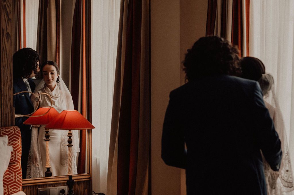 Bride and groom reflected in mirror during intimate wedding preparation moment indoors.