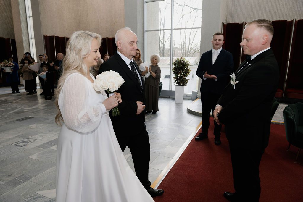 Elegant wedding ceremony with bride in white dress and groom in black suit exchanging vows indoors.