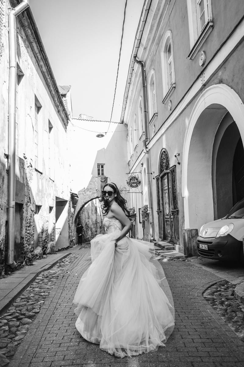 A bride in a flowing white wedding gown twirls gracefully on a cobblestone street lined with historic buildings.