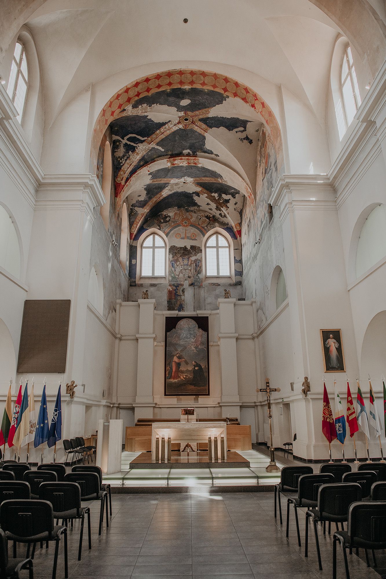 Interior view of a historic church sanctuary with white walls, arched ceilings, and rows of black chairs facing the altar.