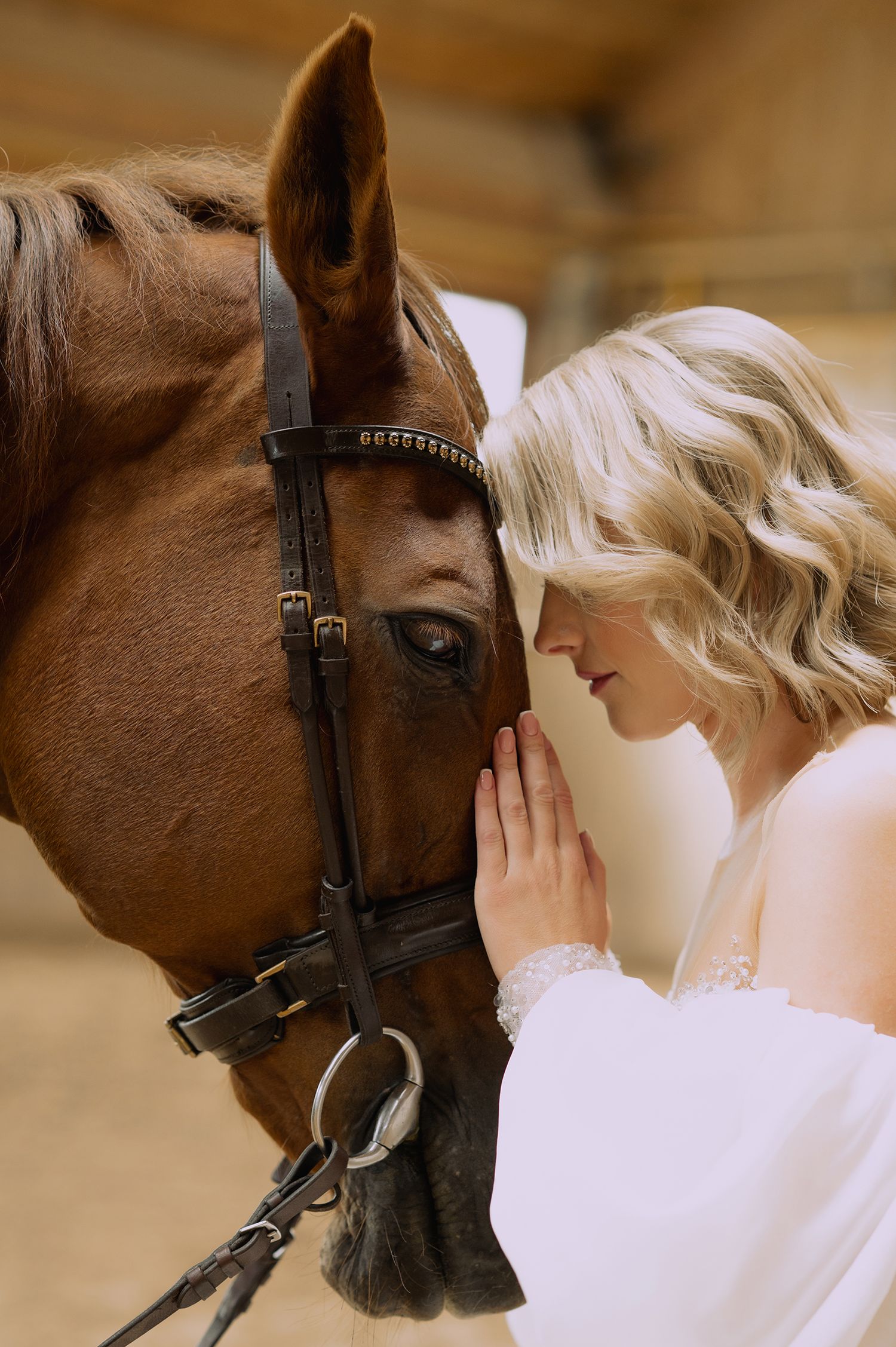 A woman in a white dress gently nuzzles a brown horse's face in a tender moment.