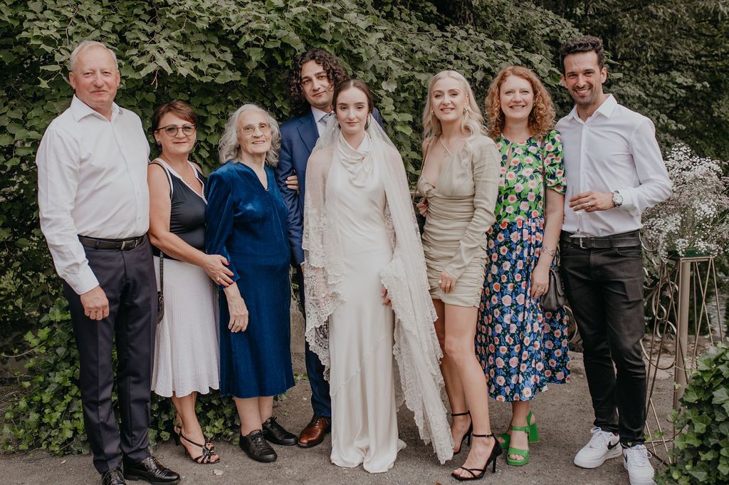 Group of eight people posing together at a wedding outdoors, bride in white gown with veil surrounded by family.