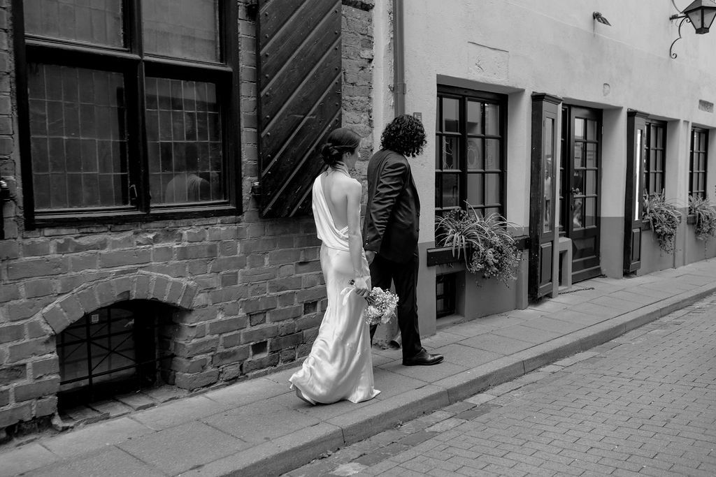 Bride and groom walk hand in hand down charming cobblestone street in black and white wedding photo.