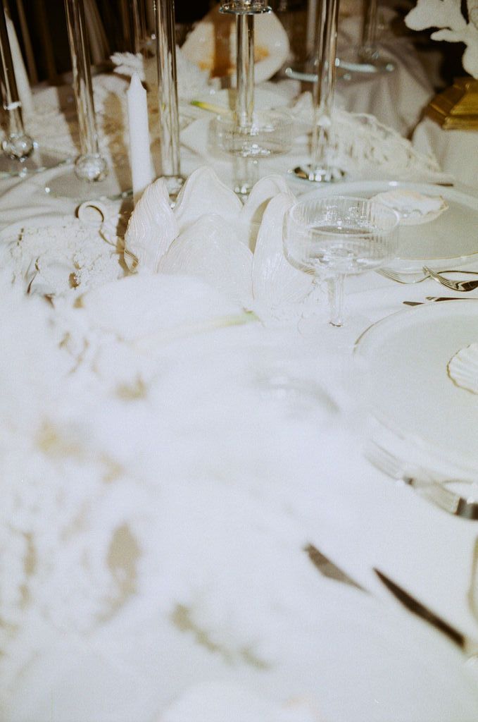 Elegant white wedding table setting with crystal glassware, white plates, candles, and delicate floral decorations.