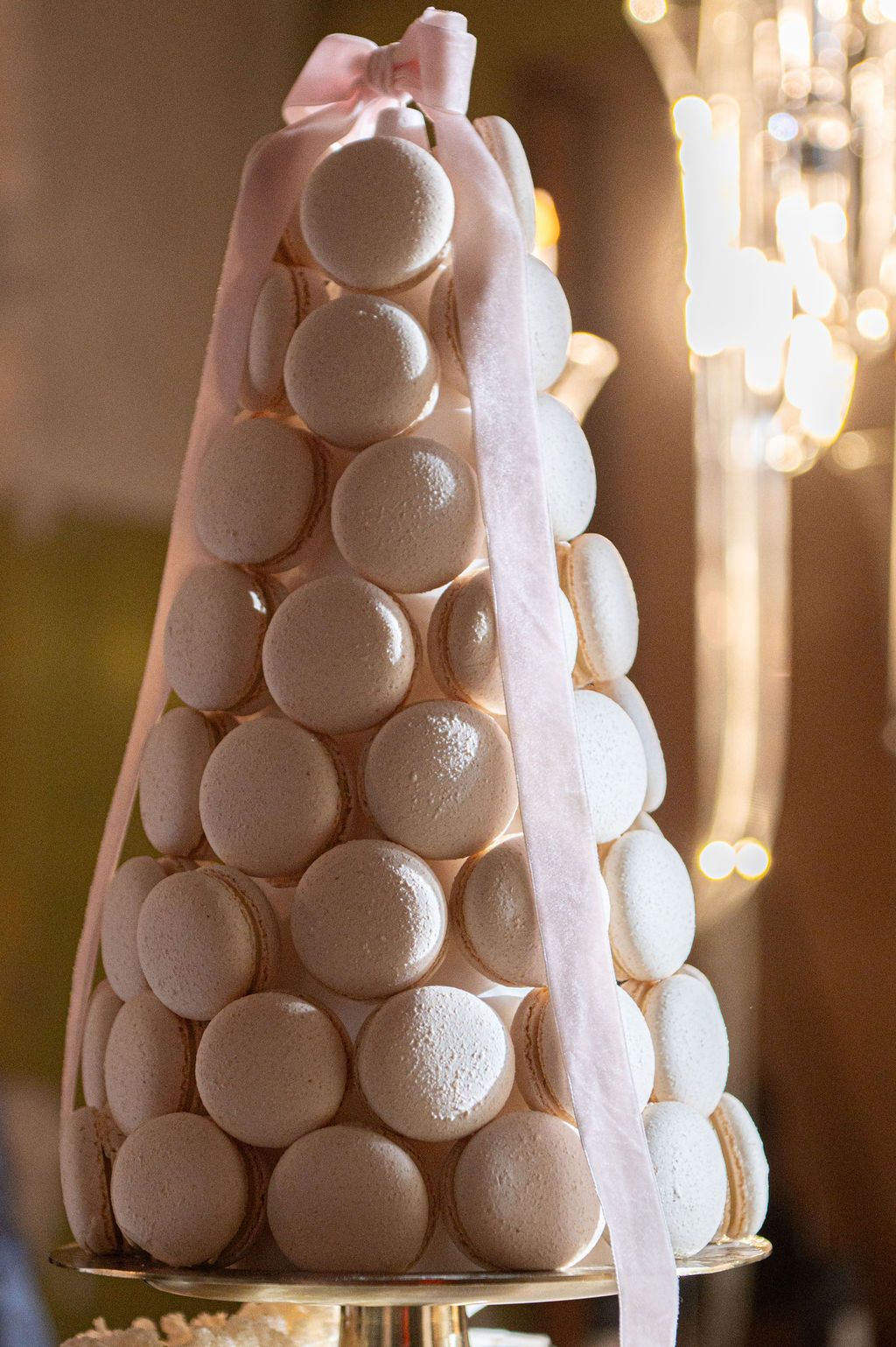 Elegant macaron tower wedding cake decorated with a pink ribbon bow, displayed on a gold stand.