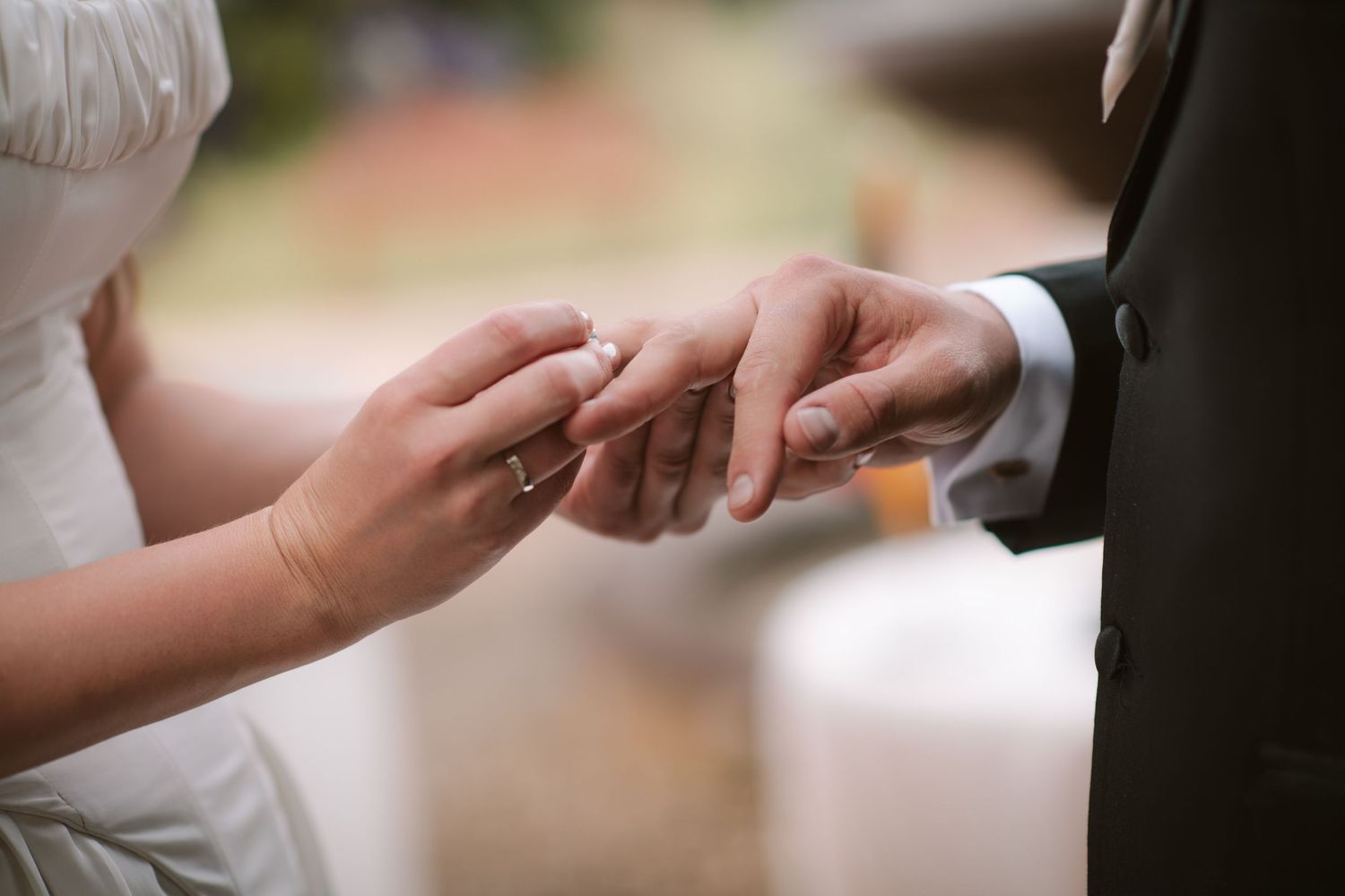 Bride placing a wedding ring on groom's finger during a romantic outdoor wedding ceremony.