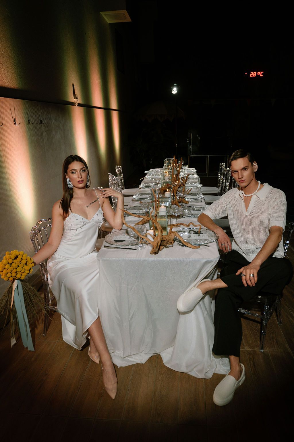 Elegant couple in formal attire seated at a decorated wedding reception table with golden centerpiece.