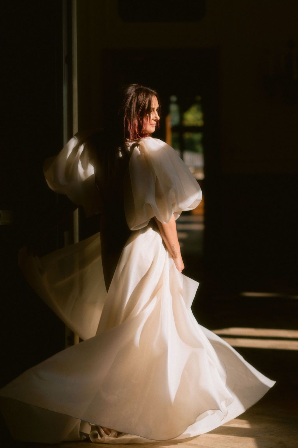 Bride in a flowing white gown with puffy sleeves twirling in golden sunlight.