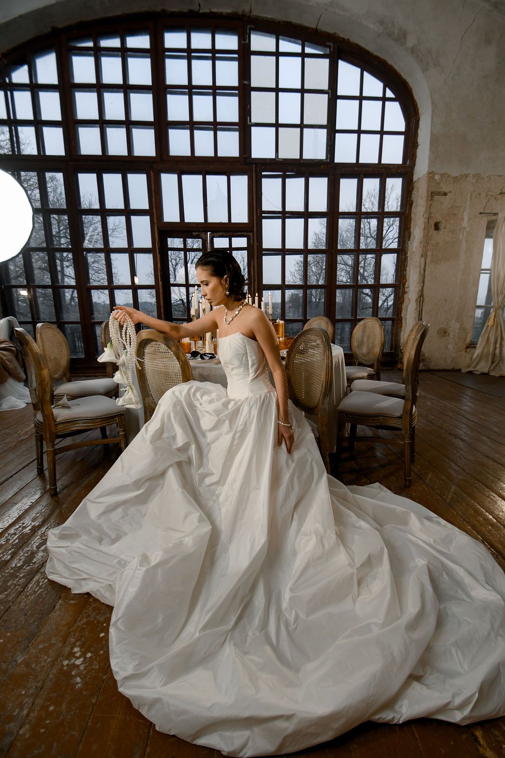Elegant bride in a strapless white ball gown with long train poses near vintage chairs in a rustic venue.
