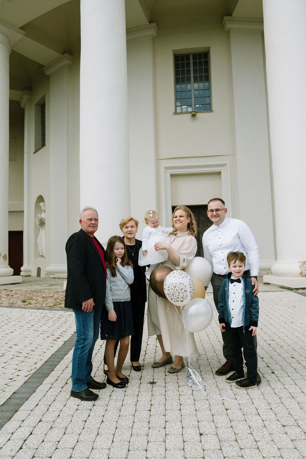 Family group photo with balloons outside a white neoclassical building, celebrating a special occasion together.
