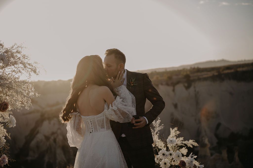 Bride and groom sharing a romantic kiss at golden hour with stunning rocky landscape backdrop at outdoor wedding.