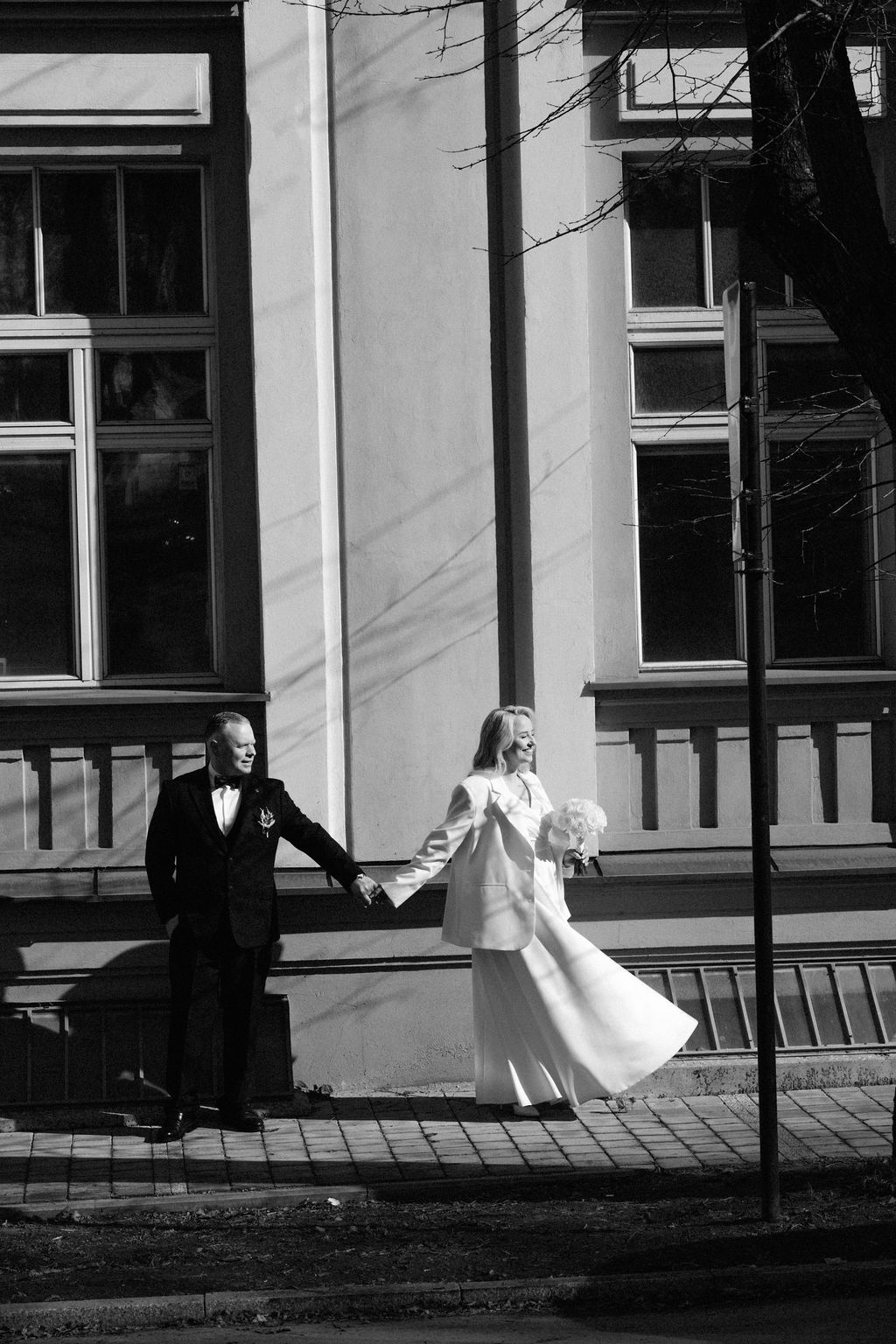 Black and white photo of a bride and groom holding hands walking outside a classic building on their wedding day.