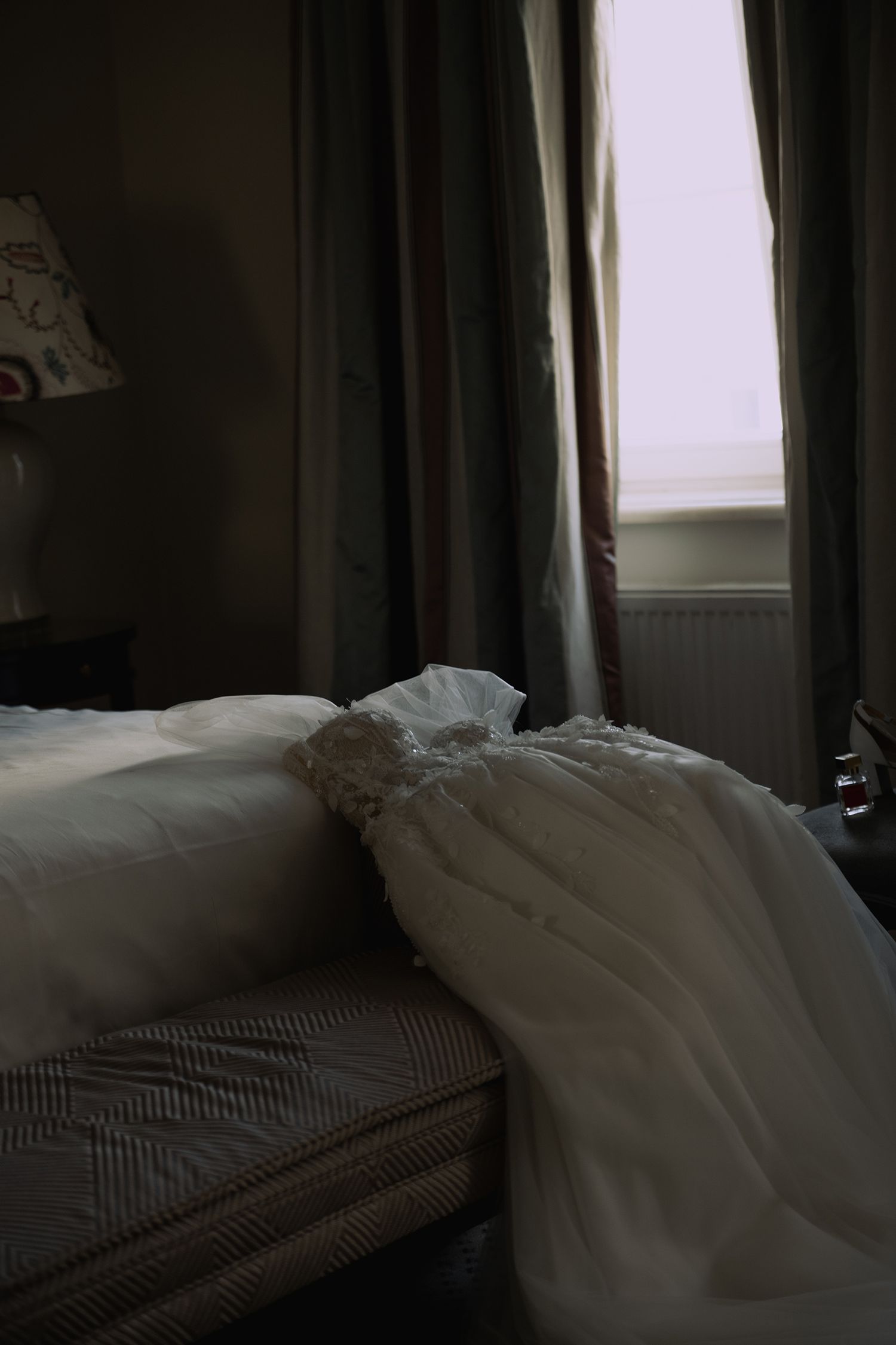 Unmade bed with rumpled white sheets and gray striped pillows in a dimly lit bedroom.