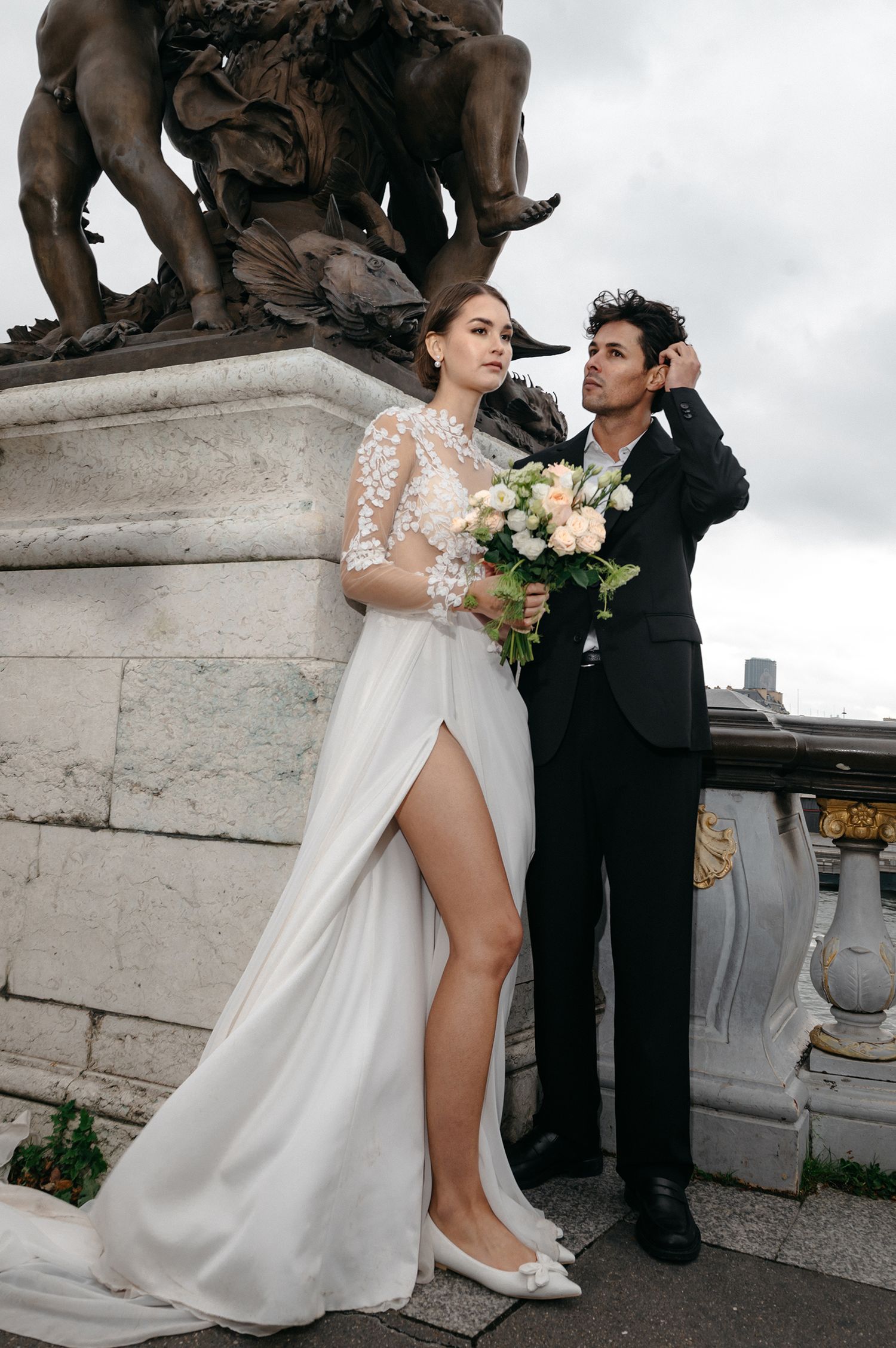 Romantic wedding couple poses on an ornate stone bridge with elegant statues in Paris.