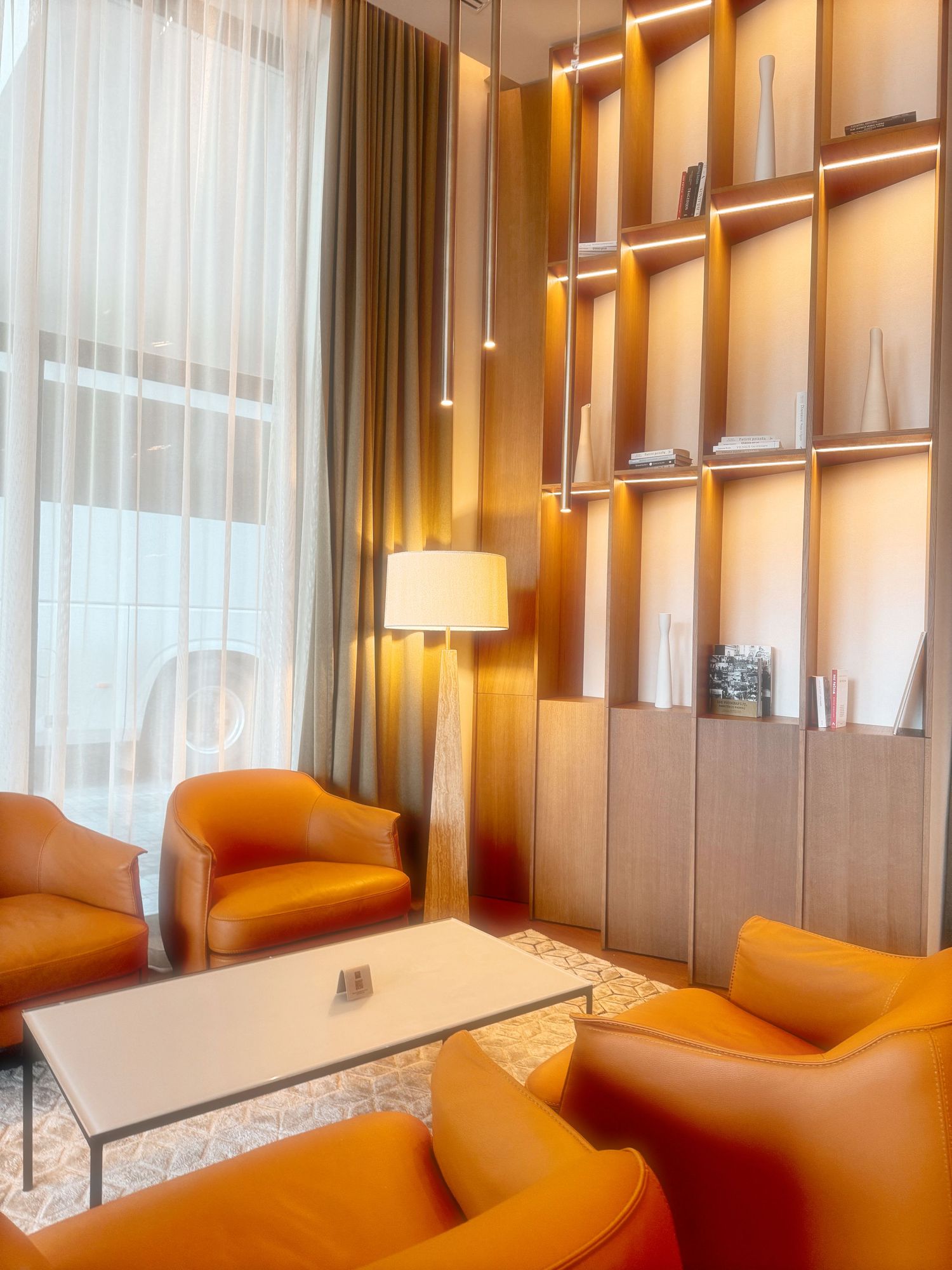 Modern hotel room interior with orange accent chairs and floor-to-ceiling windows creating a warm, luxurious ambiance.