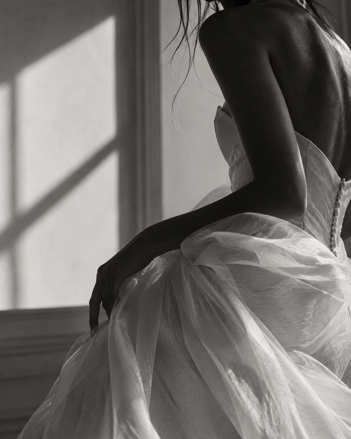 Black and white photo of a bride in a flowing white tulle gown, seated gracefully in soft natural light.