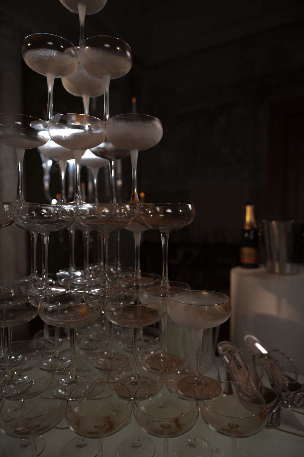 Elegant champagne tower with stacked coupe glasses at a formal event, with a bottle visible in the background.
