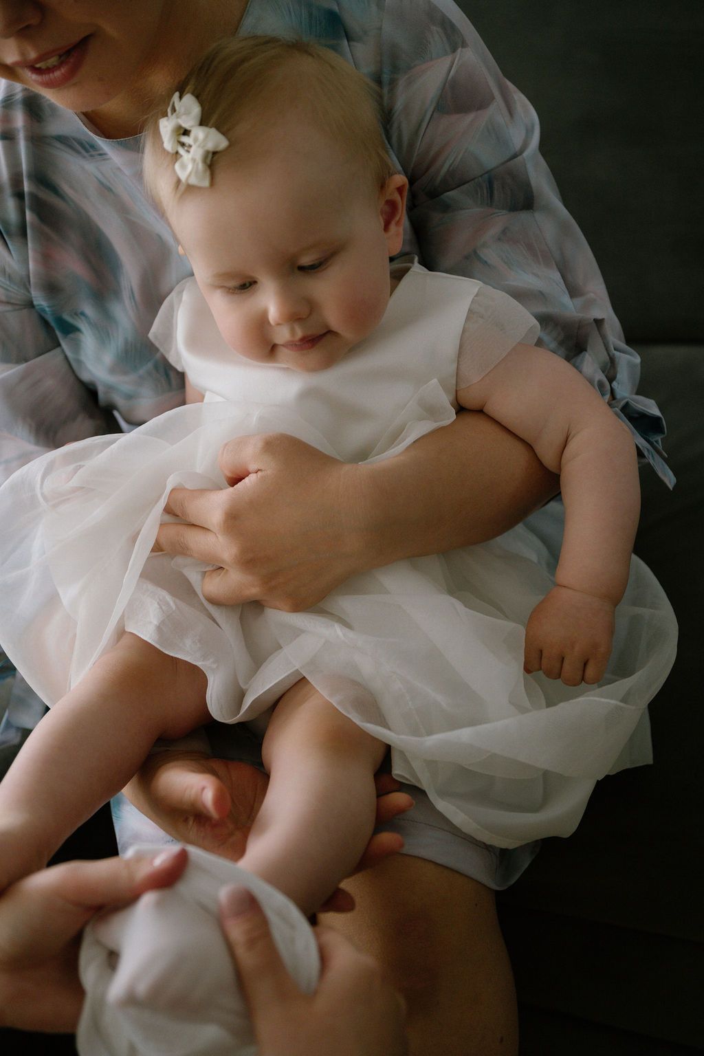 Adorable baby girl in a white tulle dress being held by a woman in a plaid shirt.