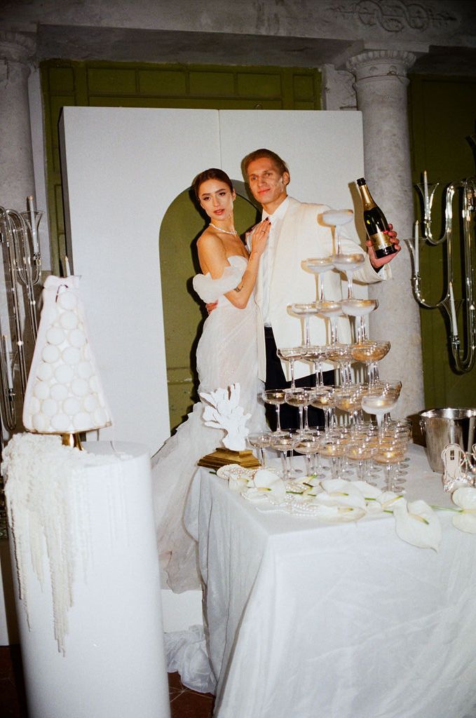 Bride and groom posing with champagne bottle next to a glass tower at their wedding.