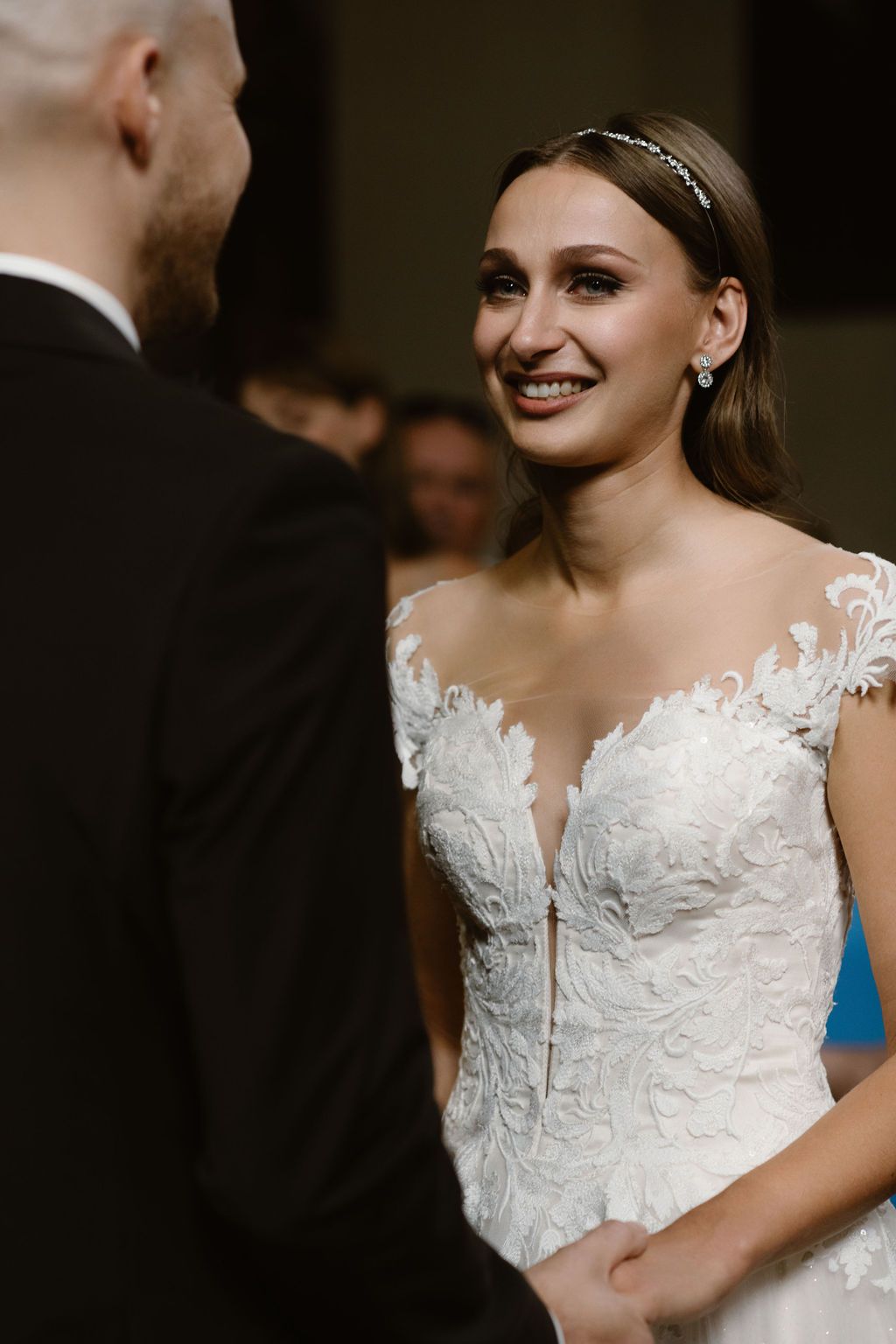Smiling bride in lace wedding gown holding hands with groom during wedding ceremony.