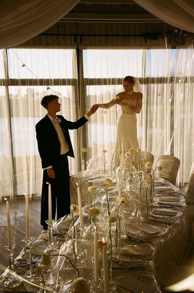 Bride and groom share a tender moment beside a stunning wedding reception table with tall candles and white florals.