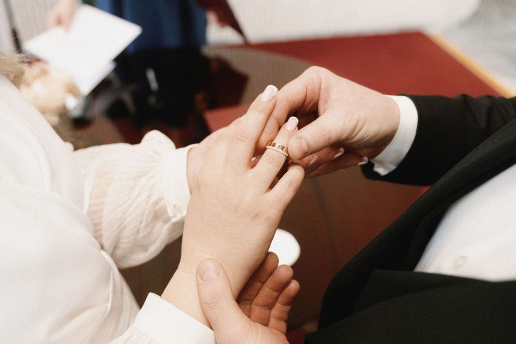 Groom placing a gold wedding ring on bride's finger during a wedding ceremony.