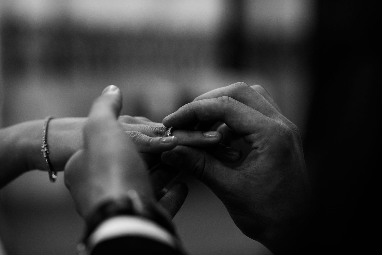 Black and white close-up of a groom sliding a wedding ring onto a bride's finger during an intimate ceremony.