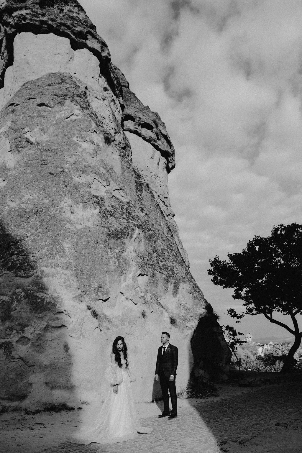 Black and white photo of bride and groom standing before a large rock formation on their wedding day.