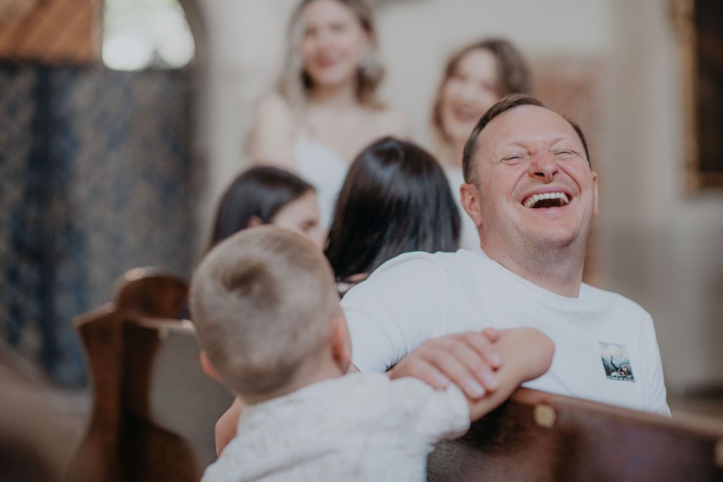 Man laughing joyfully while hugging children in a church pew during a warm family gathering.