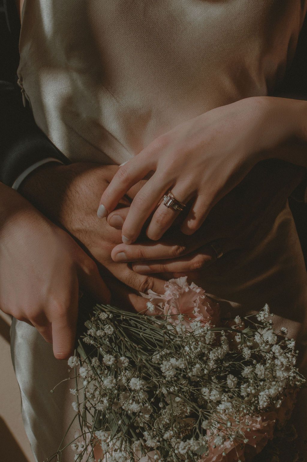 Close-up of couple holding hands with engagement ring and wedding bouquet of white and pink flowers.