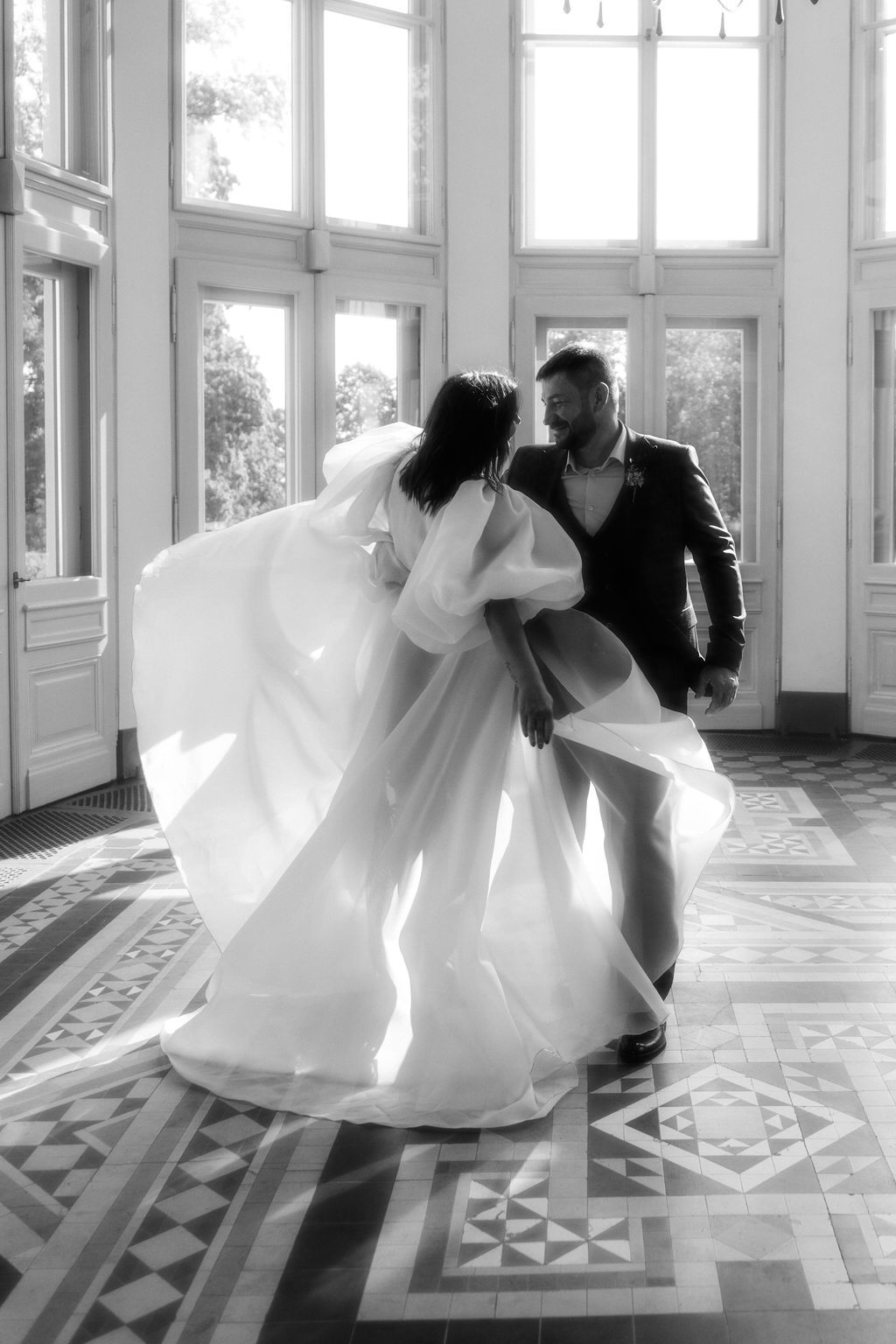 Bride and groom dancing in a sunlit ballroom, black and white wedding photo.