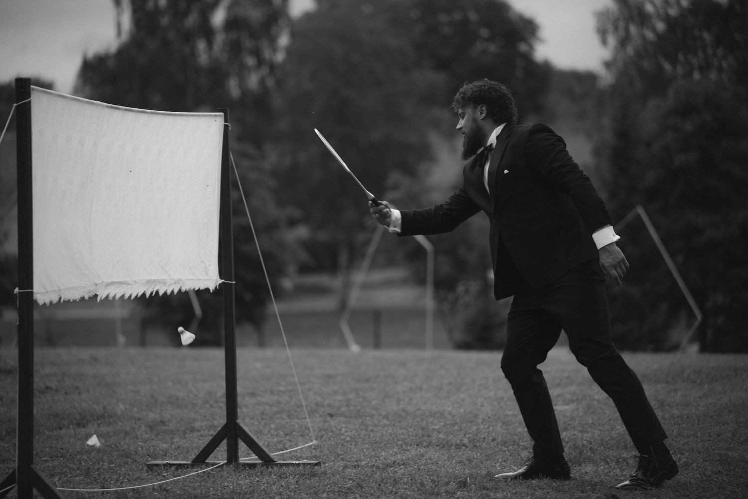 Man in suit pointing a stick at a white board on a stand in a field.