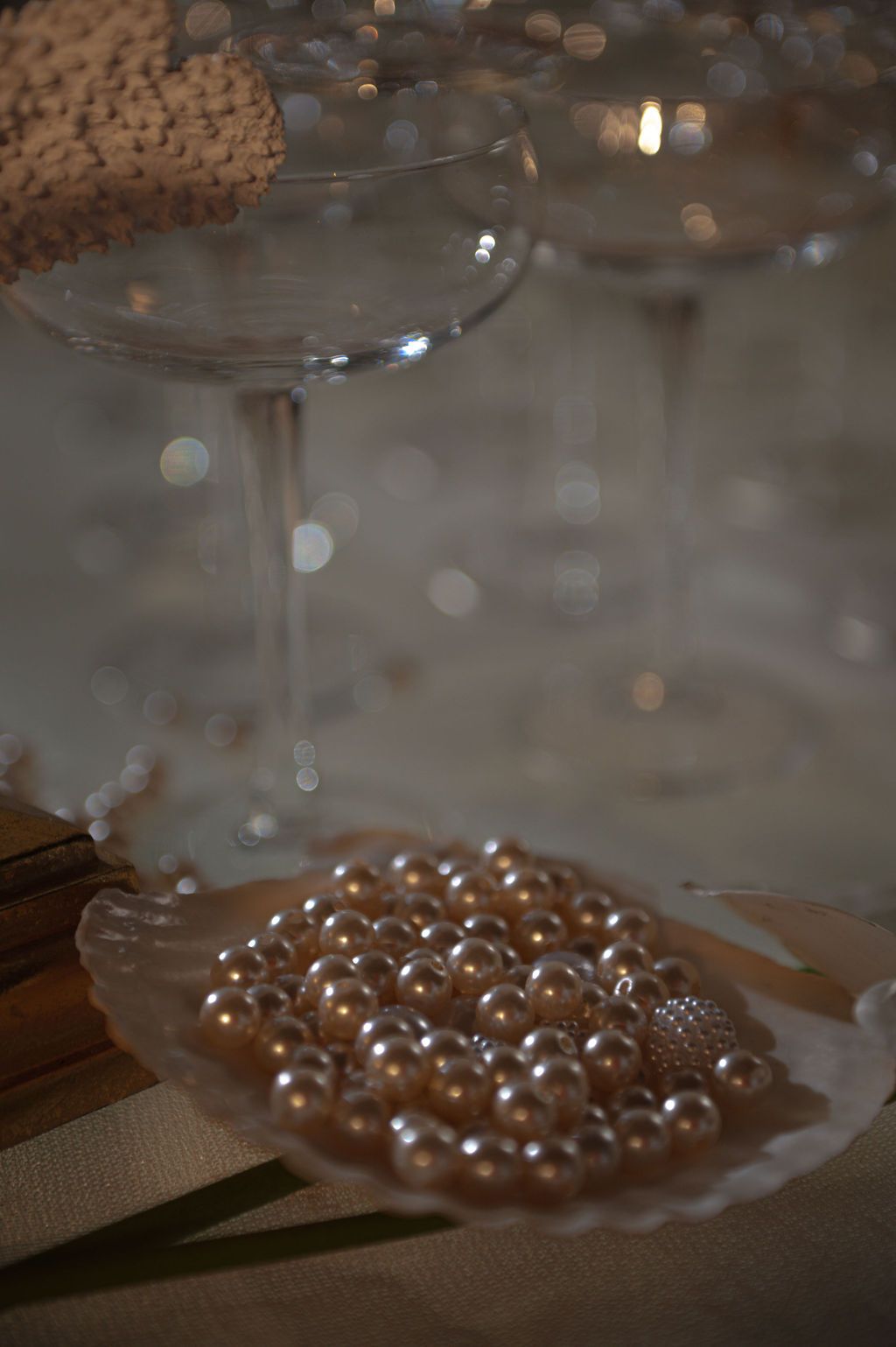 Elegant wedding table decor with pearl beads in a shell dish and champagne coupe glasses with bokeh lights.