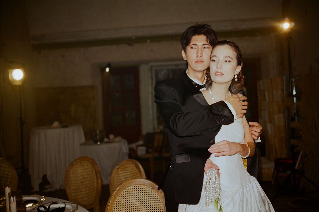 Elegant couple sharing a romantic dance embrace in a dimly lit ballroom, man in black suit, woman in white gown.