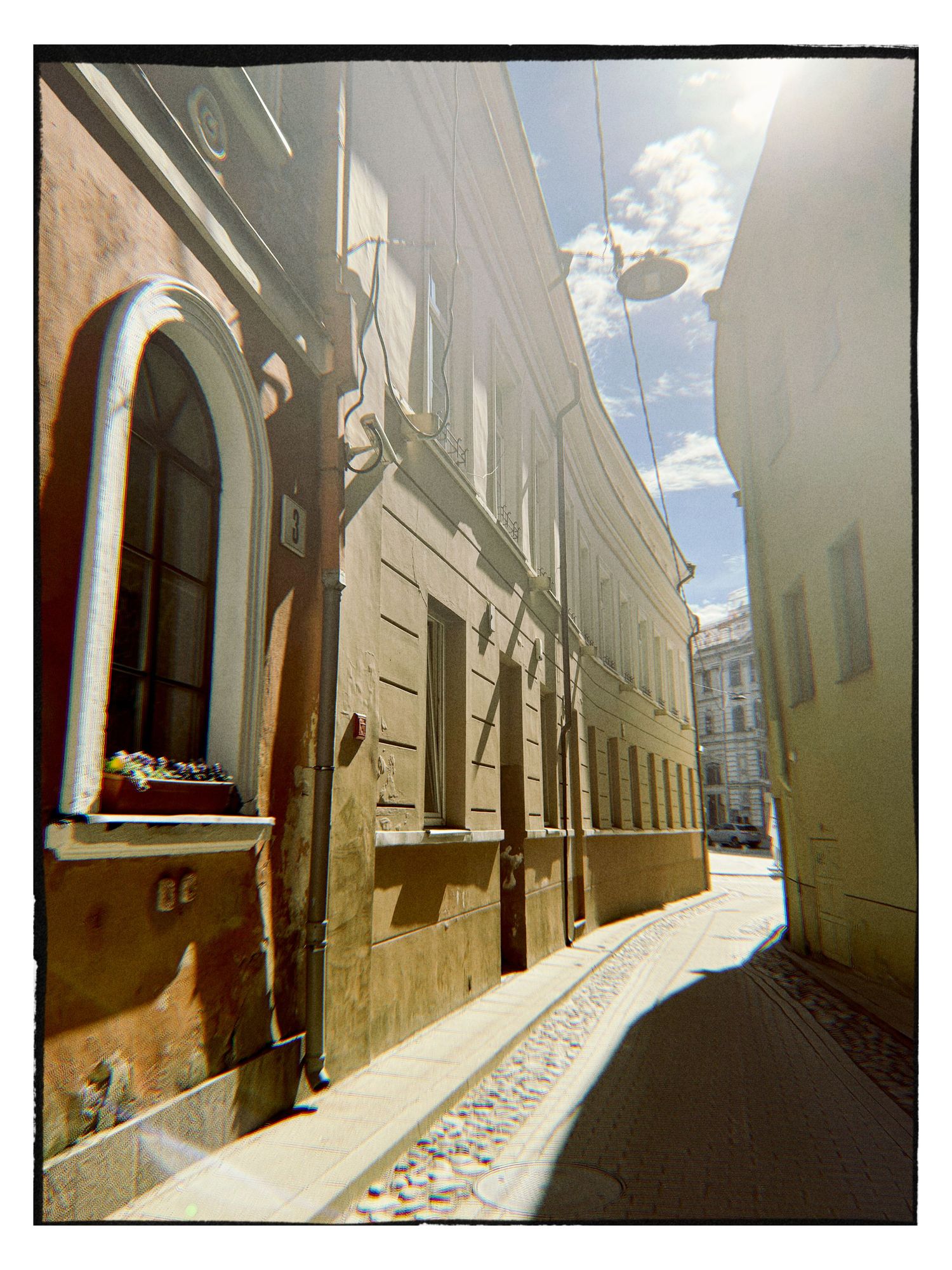 Narrow cobblestone alley flanked by historic European buildings bathed in bright sunlight on a clear day.