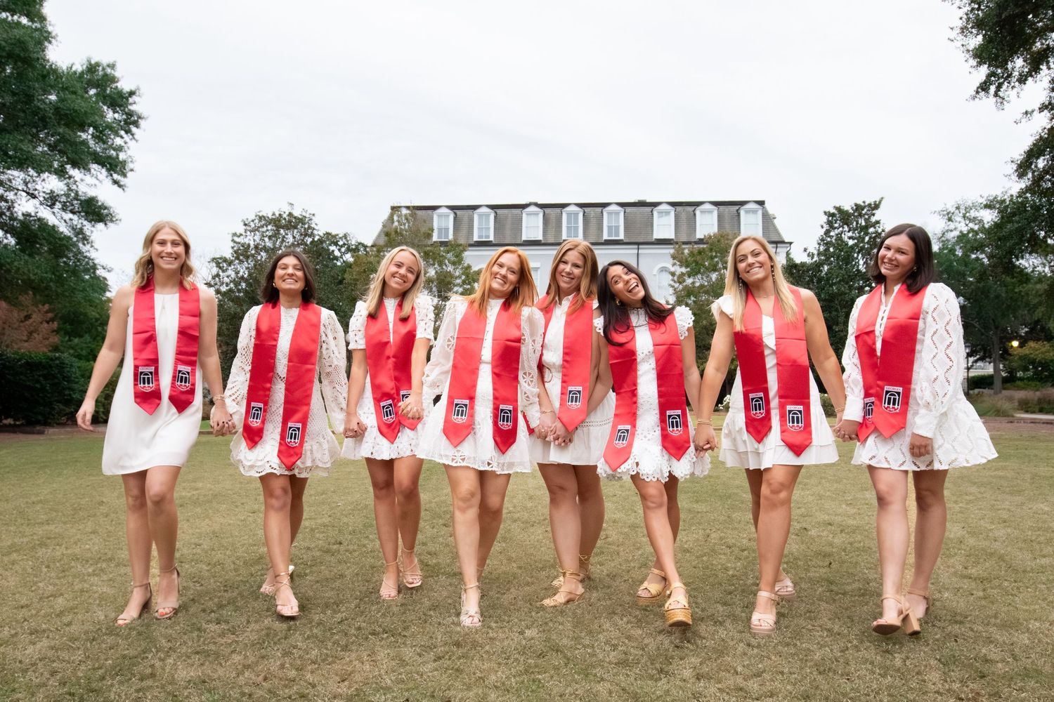 A group wearing red and white outfits poses together on a grassy lawn near a historic building.