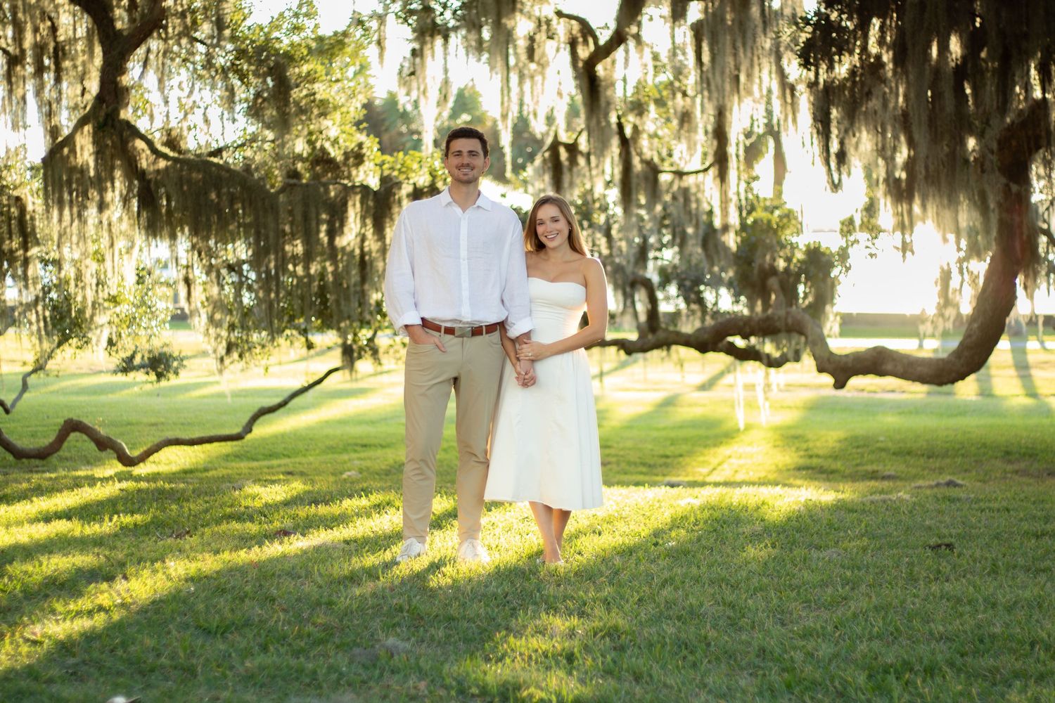 Couple walking through scenic park with Spanish moss hanging from trees at sunset.