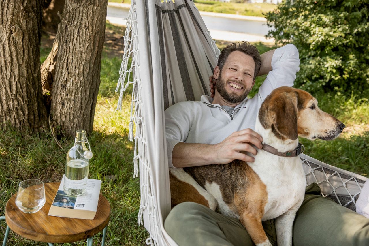 Peter Schotting enjoying a relaxed moment in a hammock with a dog, outdoor lifestyle campaign, commercial photography