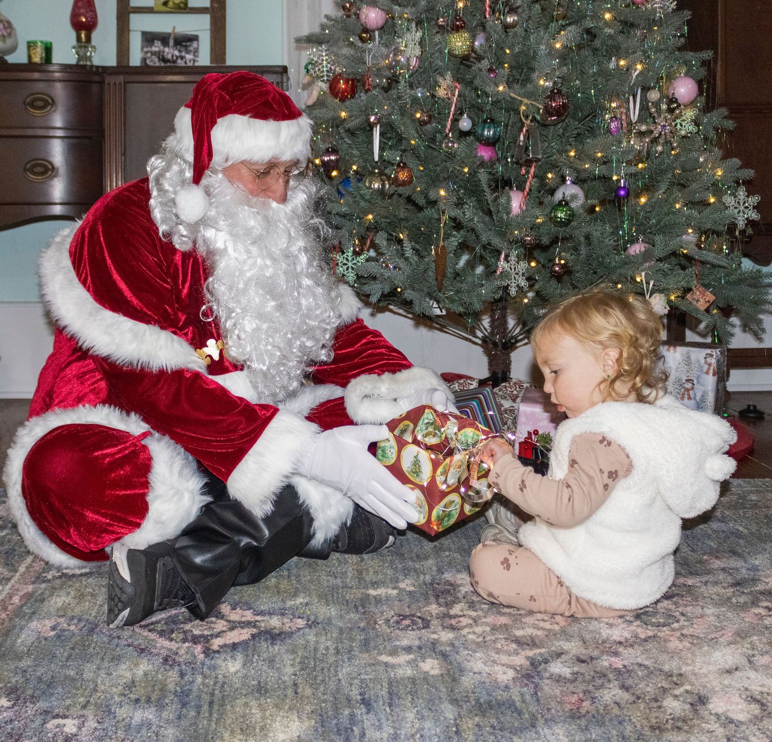 Sequence showing Santa Claus interacting with a small child by a Christmas tree.