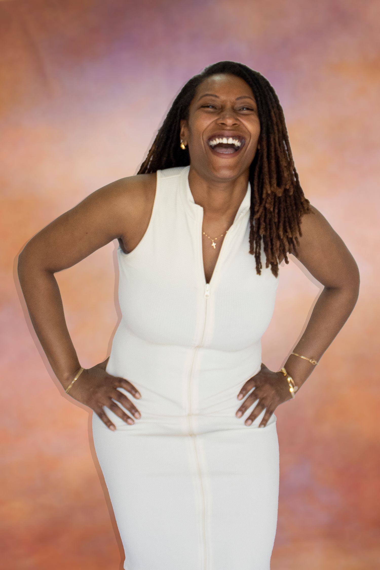 Joyful woman in white sleeveless dress with locs, hands on hips, laughing against colorful backdrop.