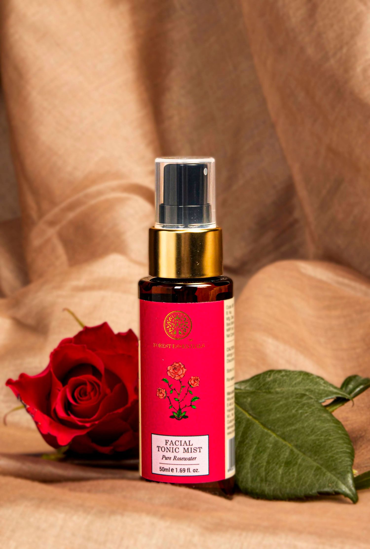 Red roses and pink beauty product containers arranged on beige fabric for product photography.