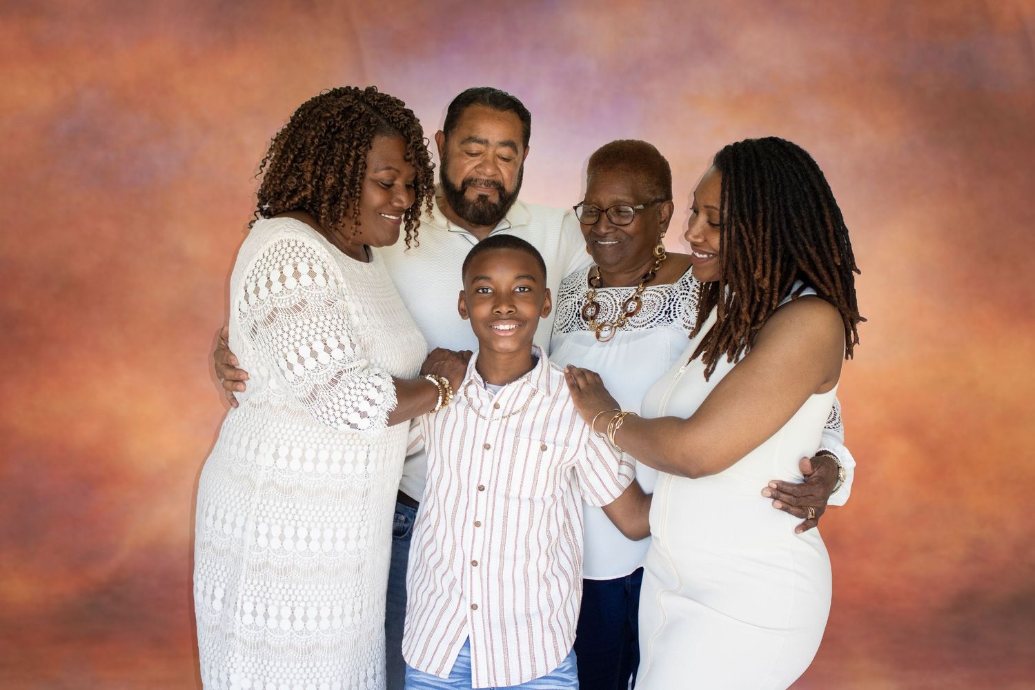 A joyful family of five in white outfits poses together against a warm studio backdrop for a professional portrait.