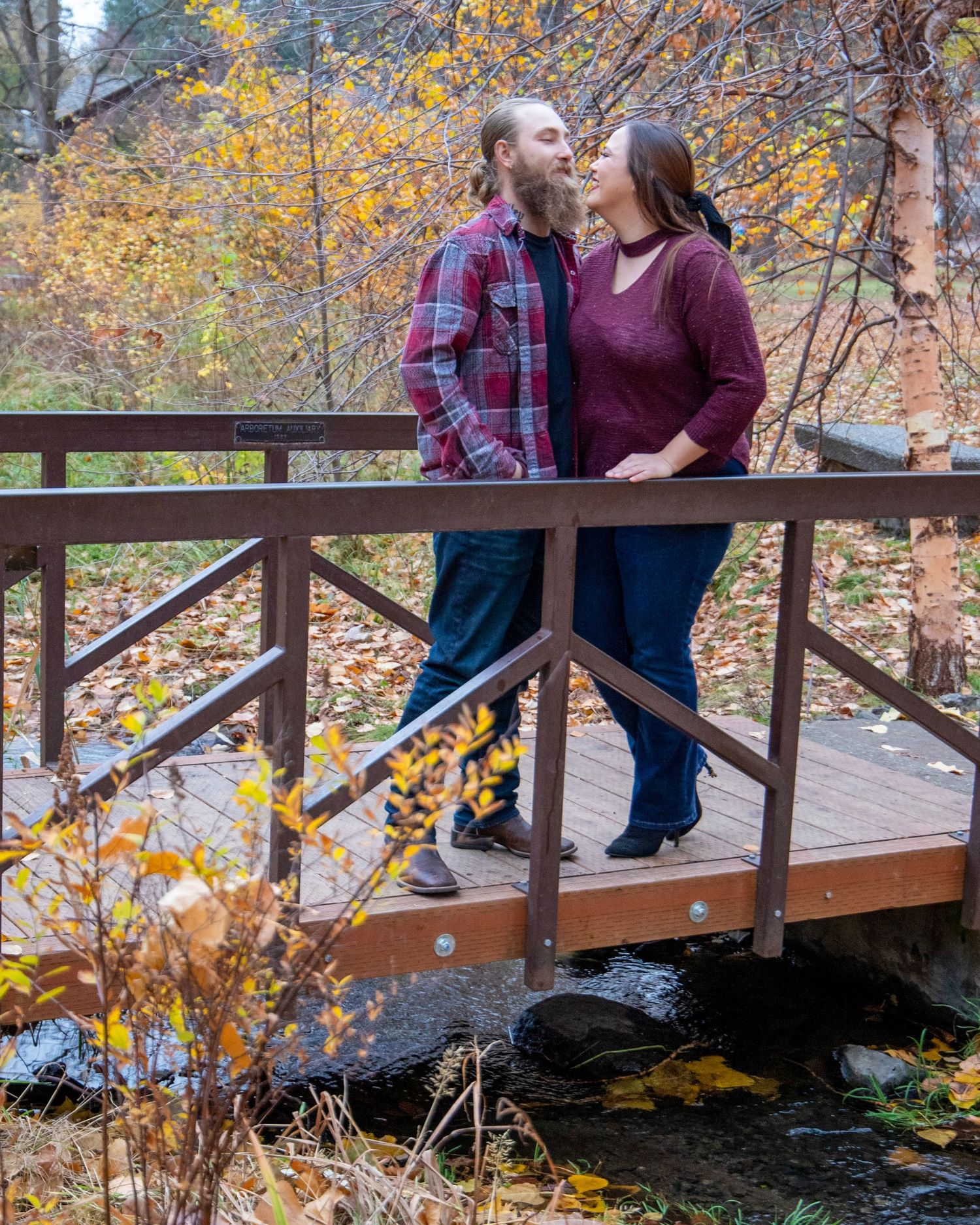 Couple walking across a wooden bridge surrounded by autumn foliage.