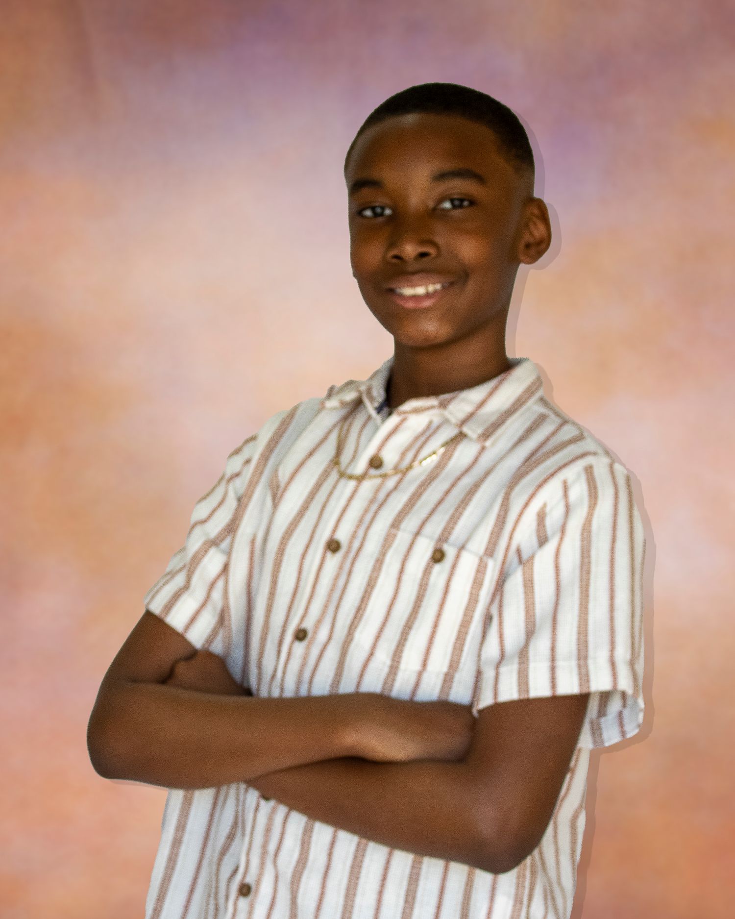 Smiling young boy with crossed arms wearing a striped button-up shirt poses for a school portrait photo.