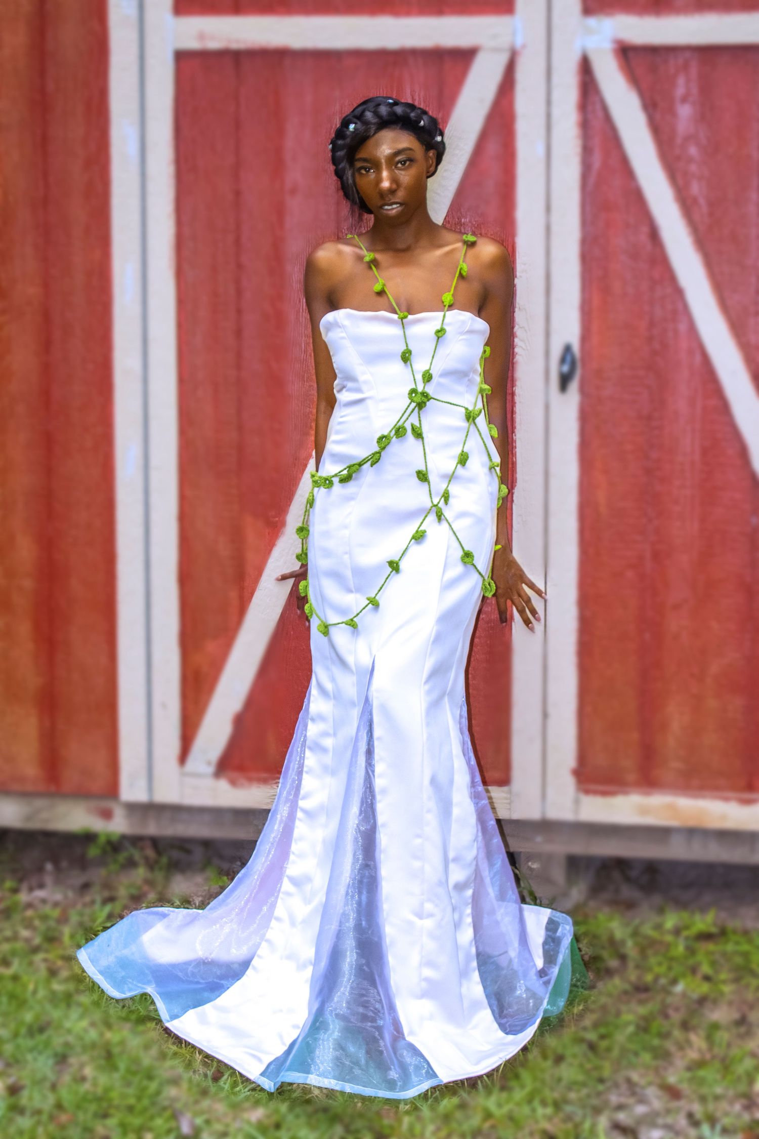 A white flowing dress with green vine details against a red barn backdrop.