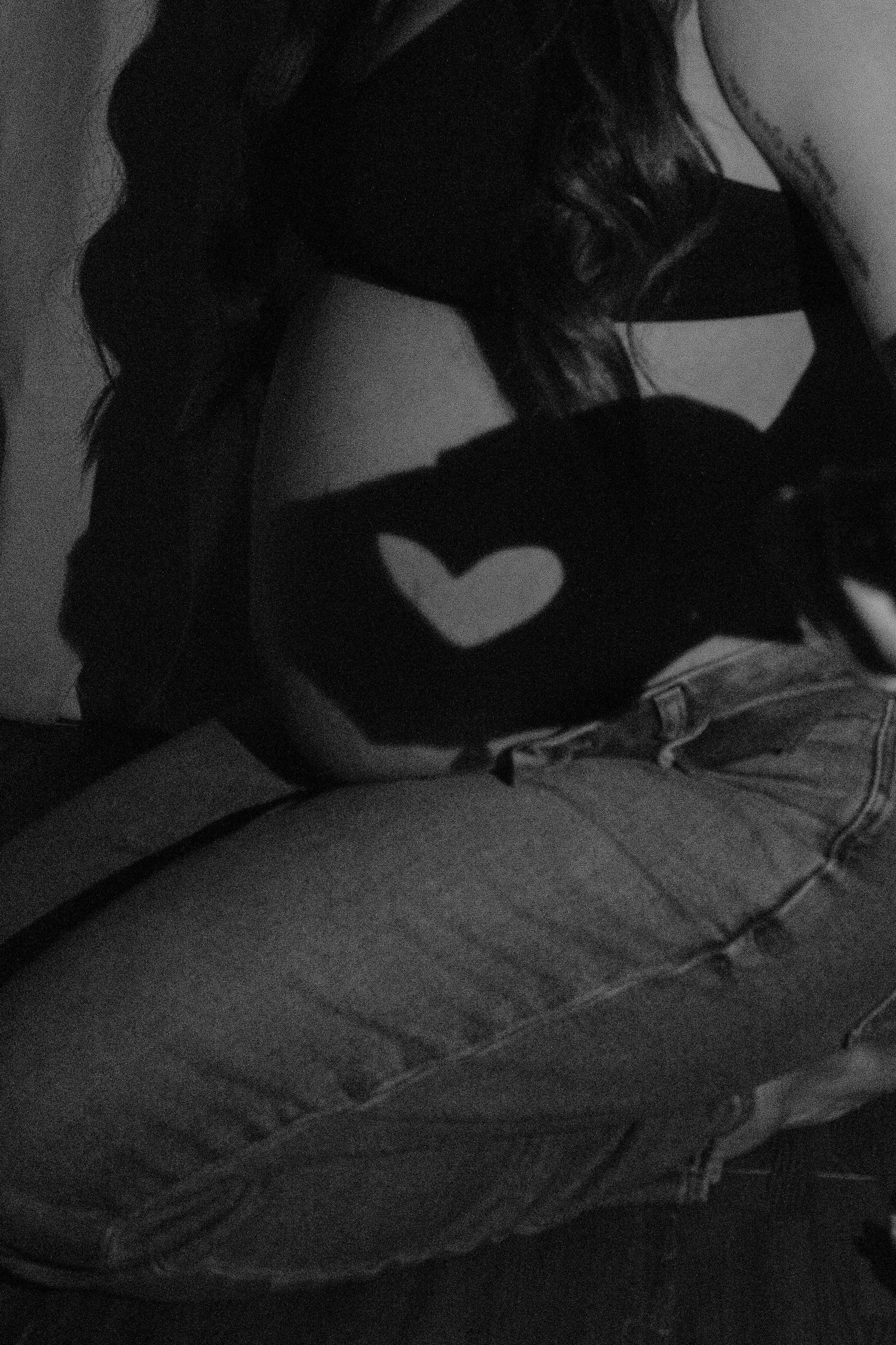 Black and white photo of pregnant woman sitting with heart-shaped shadow on baby bump wearing jeans.