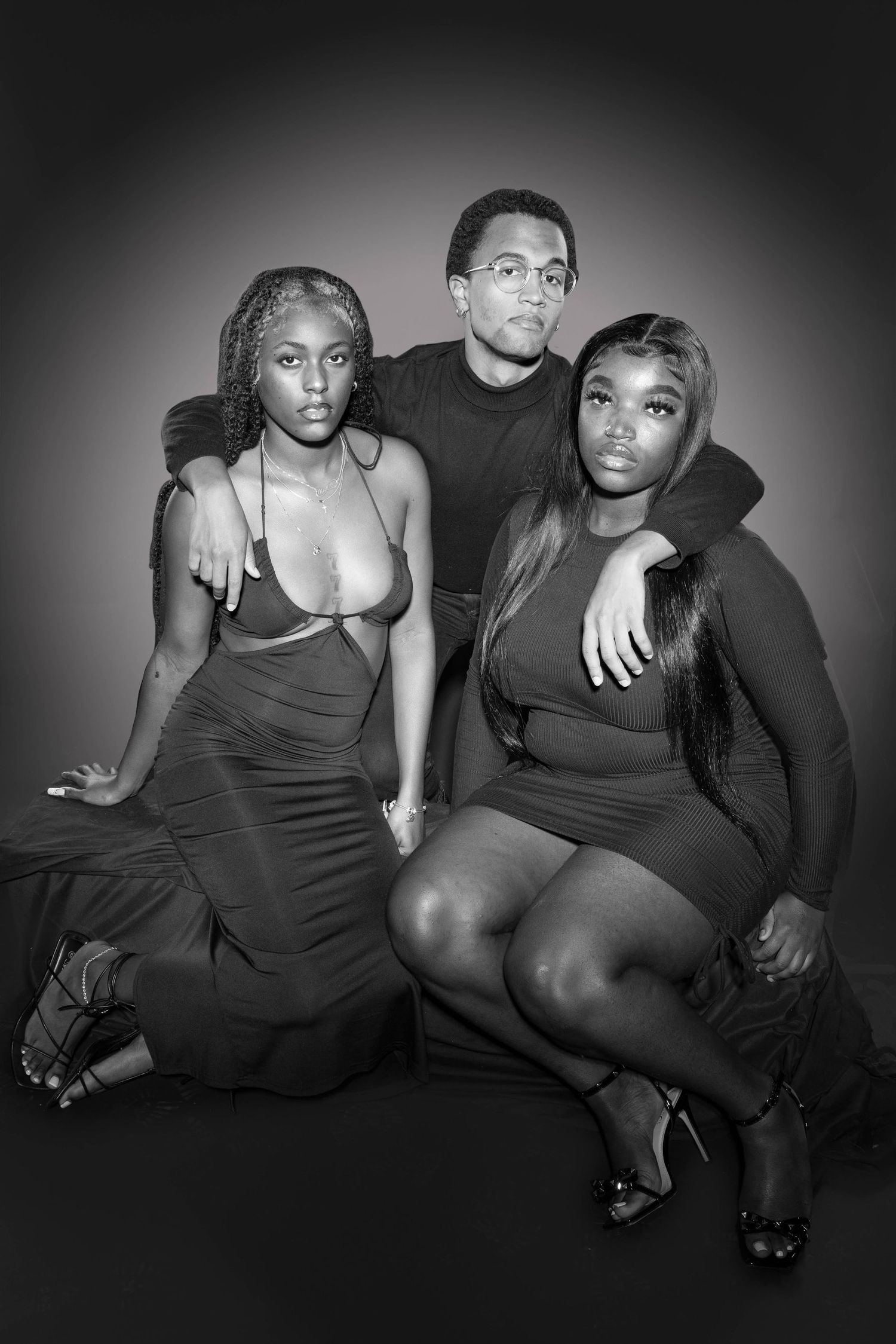 Black and white studio portrait of three young adults posing together, two women seated and one man standing behind them.